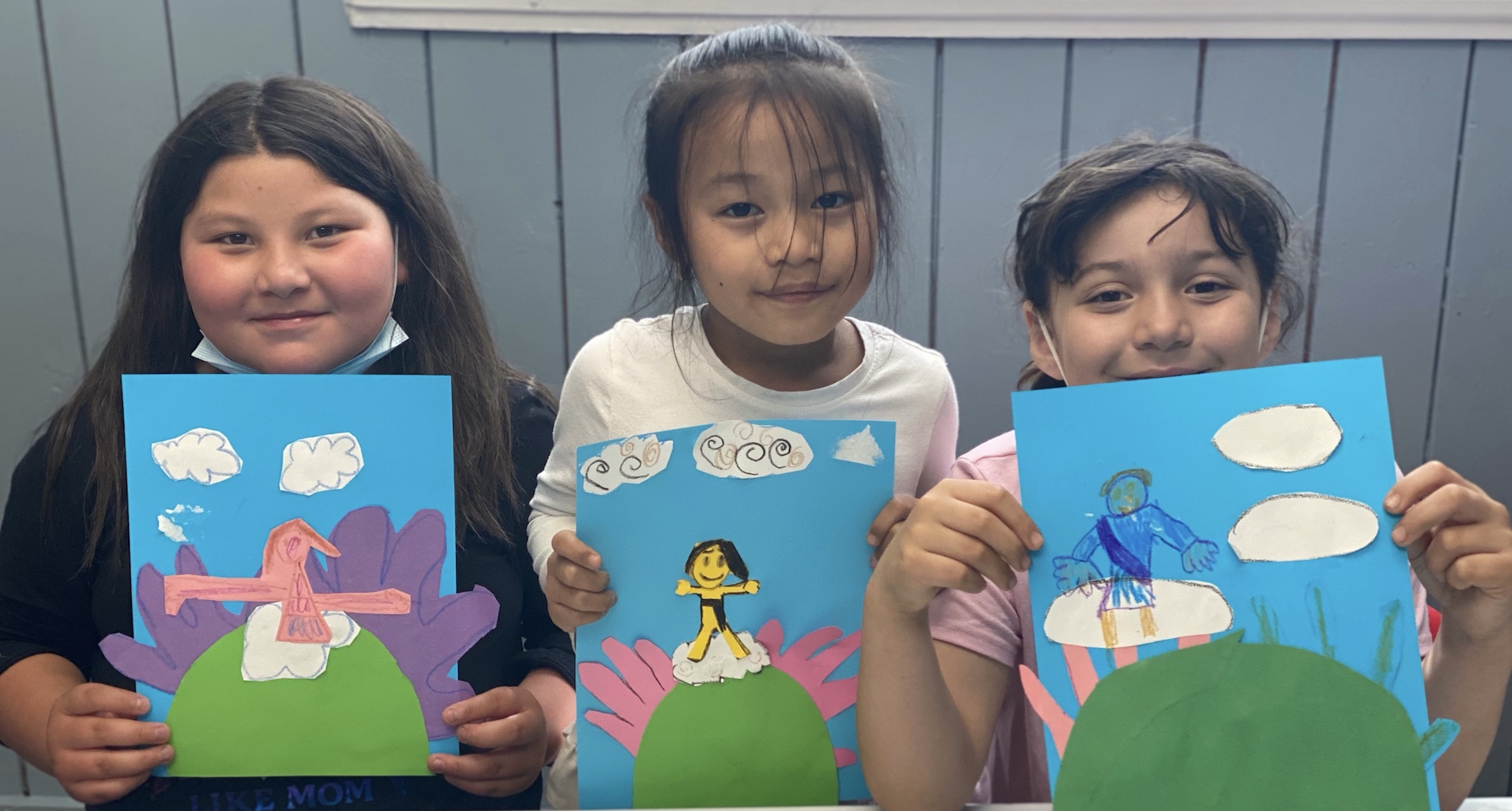three smiling girls holding paintings